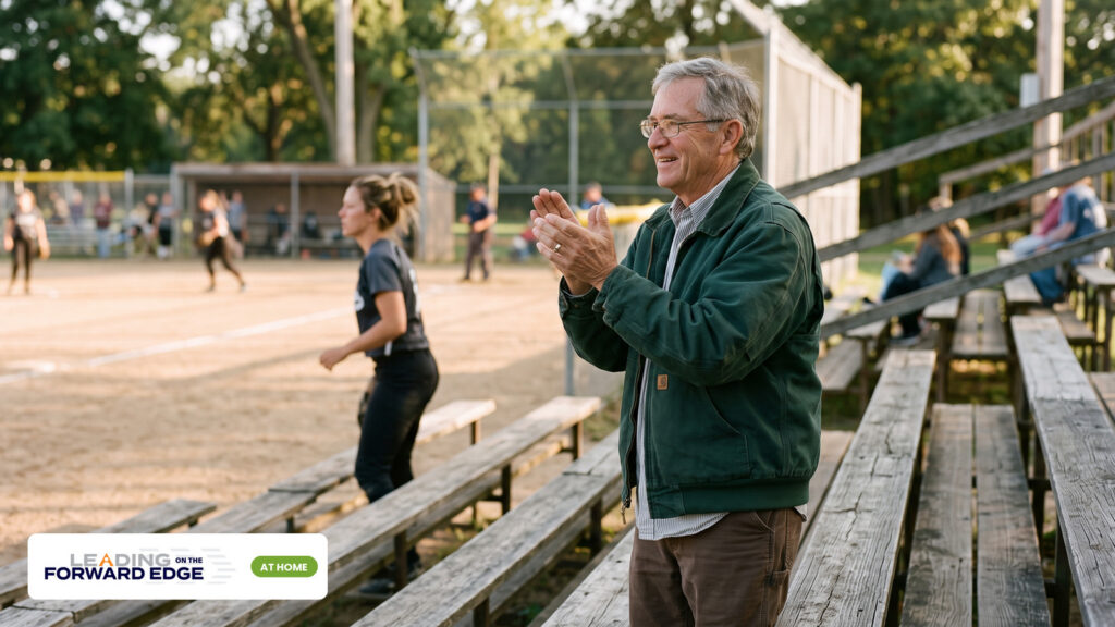 Older father standing and clapping in the bleachers for his grown daughter. Leading on the Forward Edge At Home.